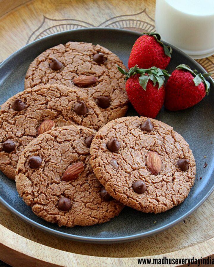 4 chocolate almond cookies placed in plate with strawberries and milk