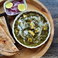 palak paneer topped with cream , chapathi, onion and lime wedges in the picture