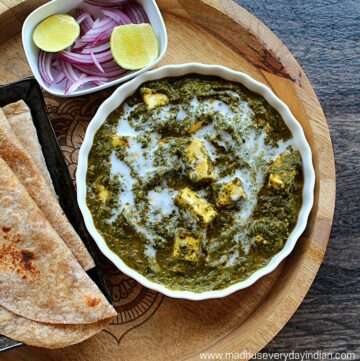 palak paneer topped with cream , chapathi, onion and lime wedges in the picture