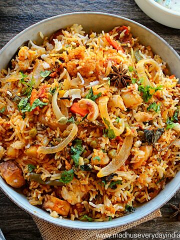 vegetable biryani served in a large bowl with raita on the side