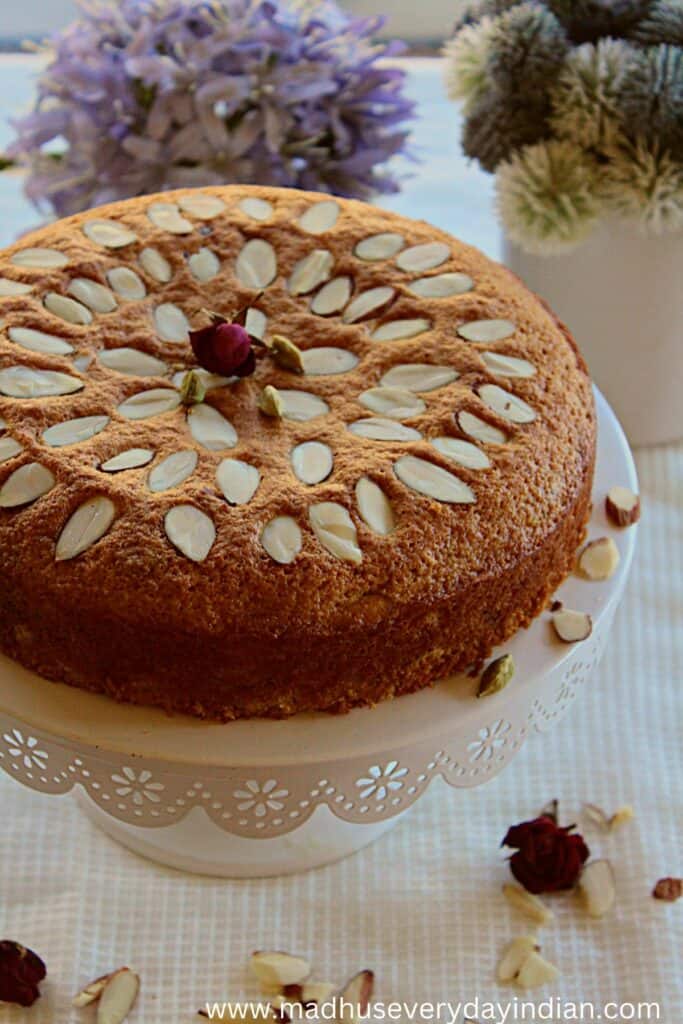 almond cake arranged in a cake tray with dry rose petals and cardamom poda
