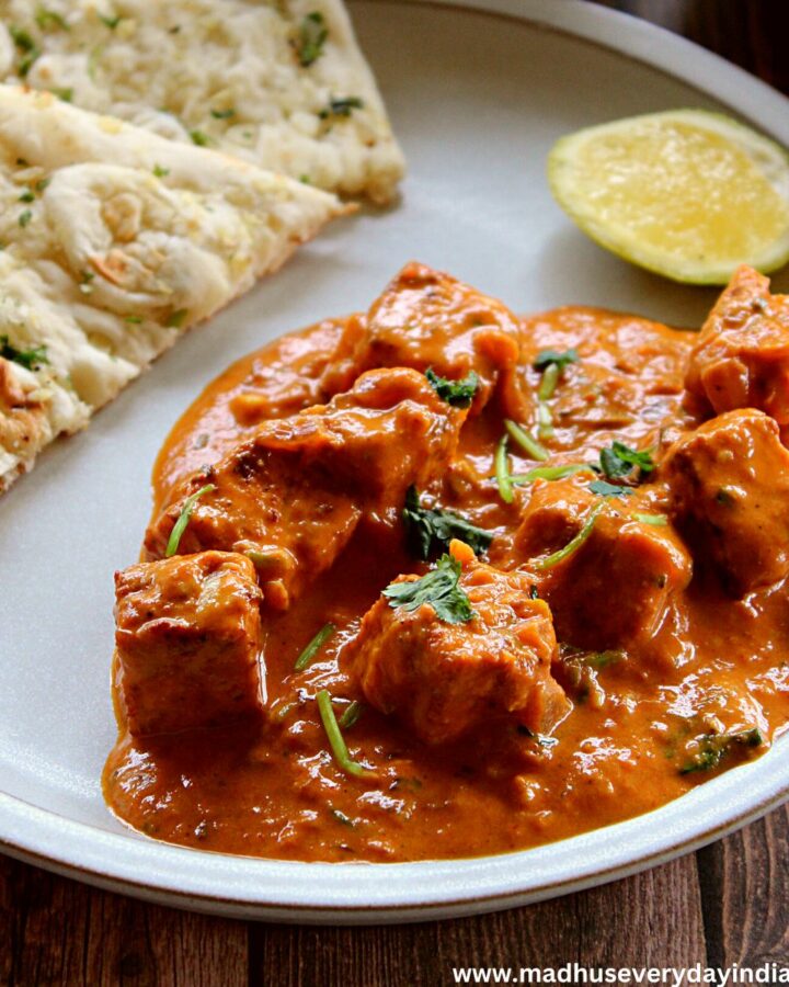 tofu tikka masala served in a white plate with naan and lemon